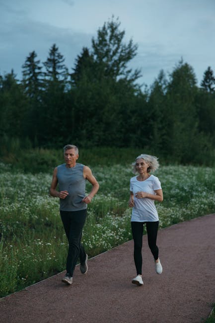 Elderly couple jogging on a serene park path surrounded by nature, enjoying outdoor exercise.