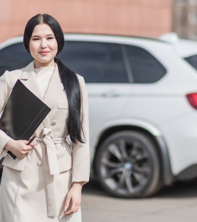 Smiling professional woman standing confidently by a luxury car, embodying success.